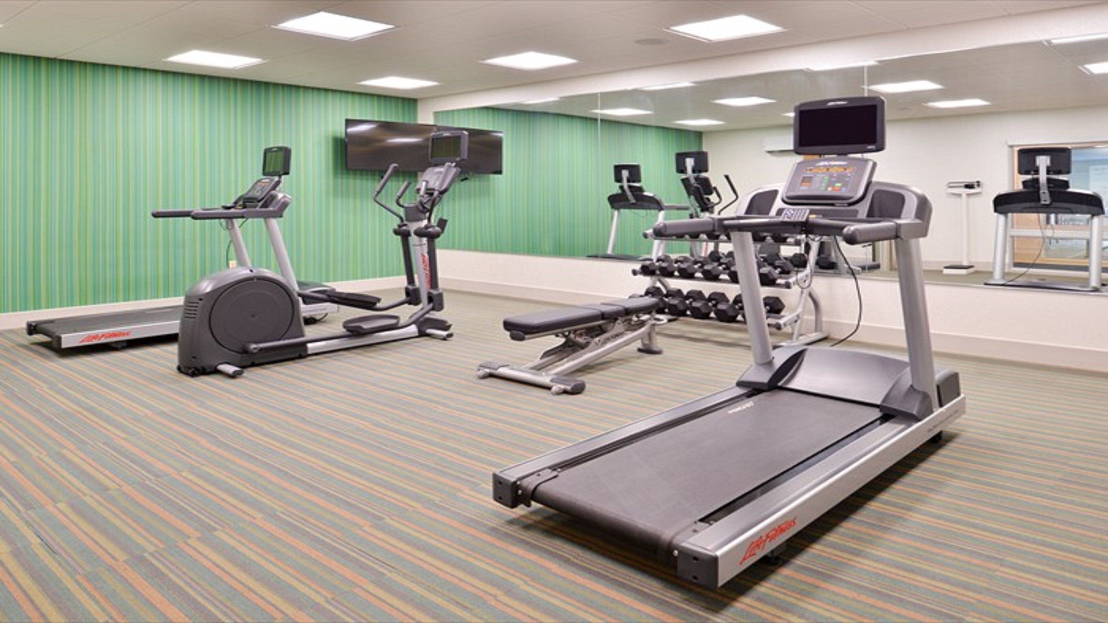 Un gimnasio con cintas de correr, elípticas y pesas libres.