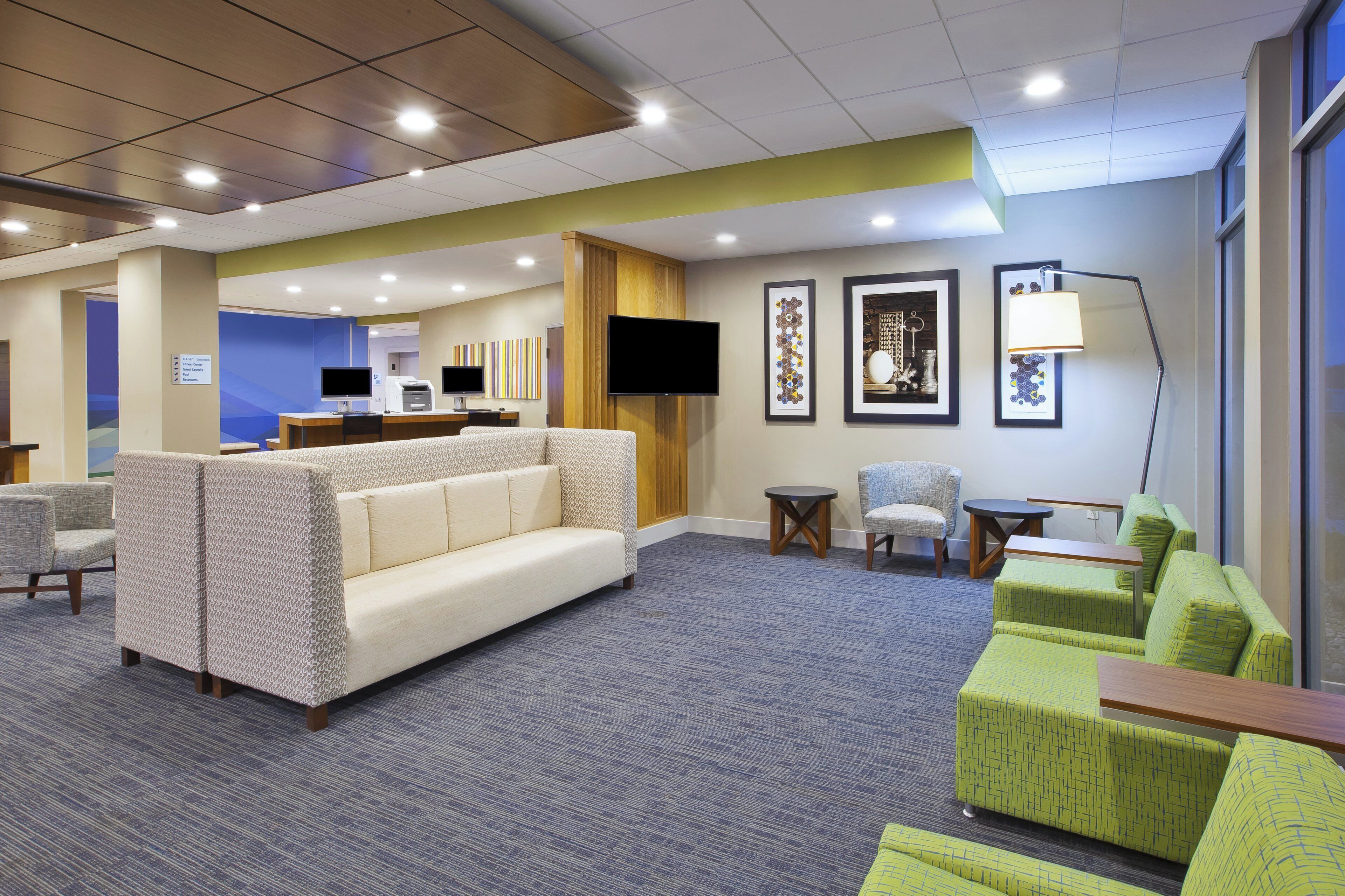 A hotel lobby with seating areas, a reception desk, and a television.