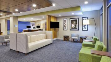 A hotel lobby with seating areas, a reception desk, and a television.