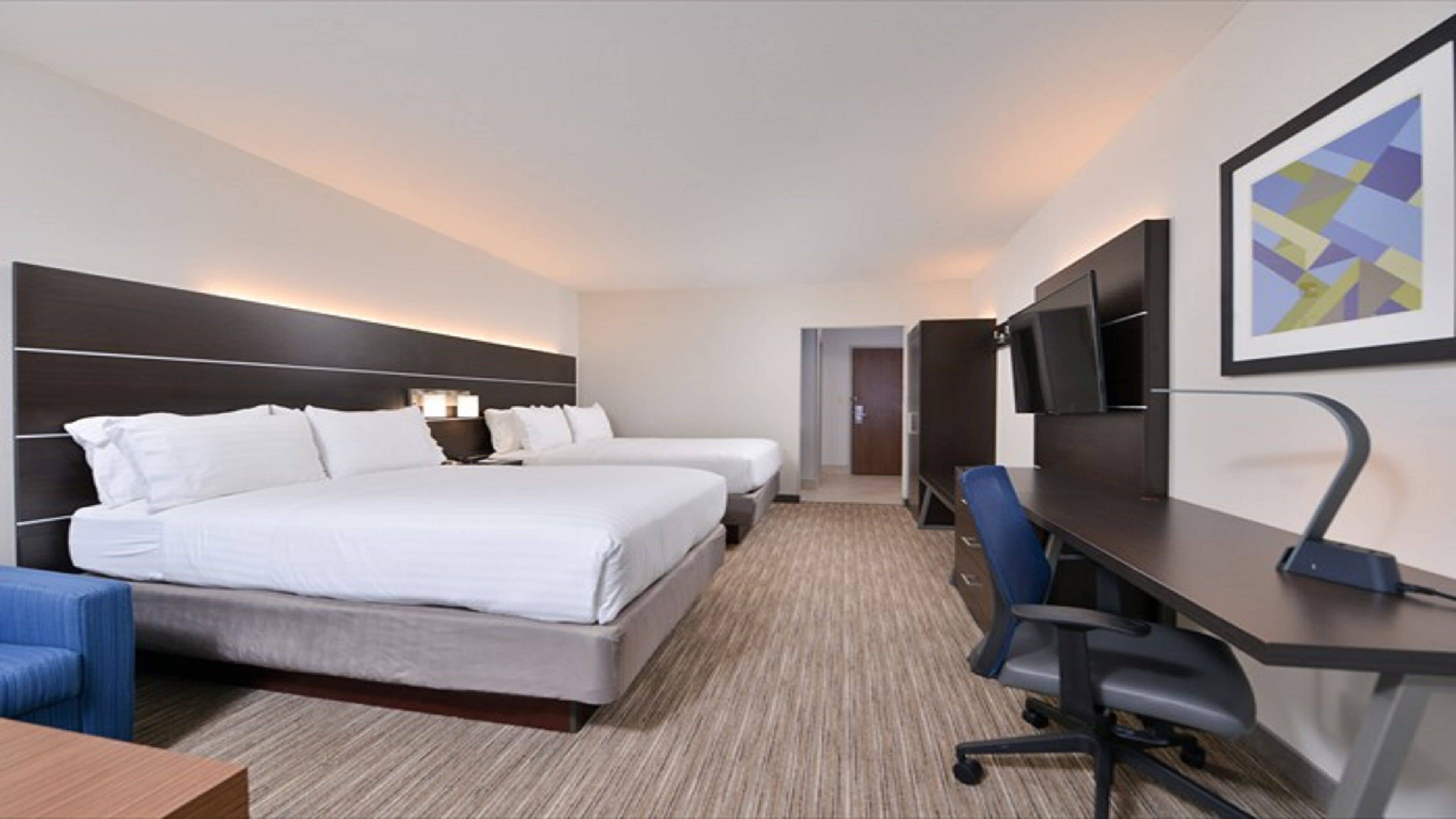 Quarto de hotel com duas camas, uma escrivaninha, uma cadeira, televisão e quadro na parede.