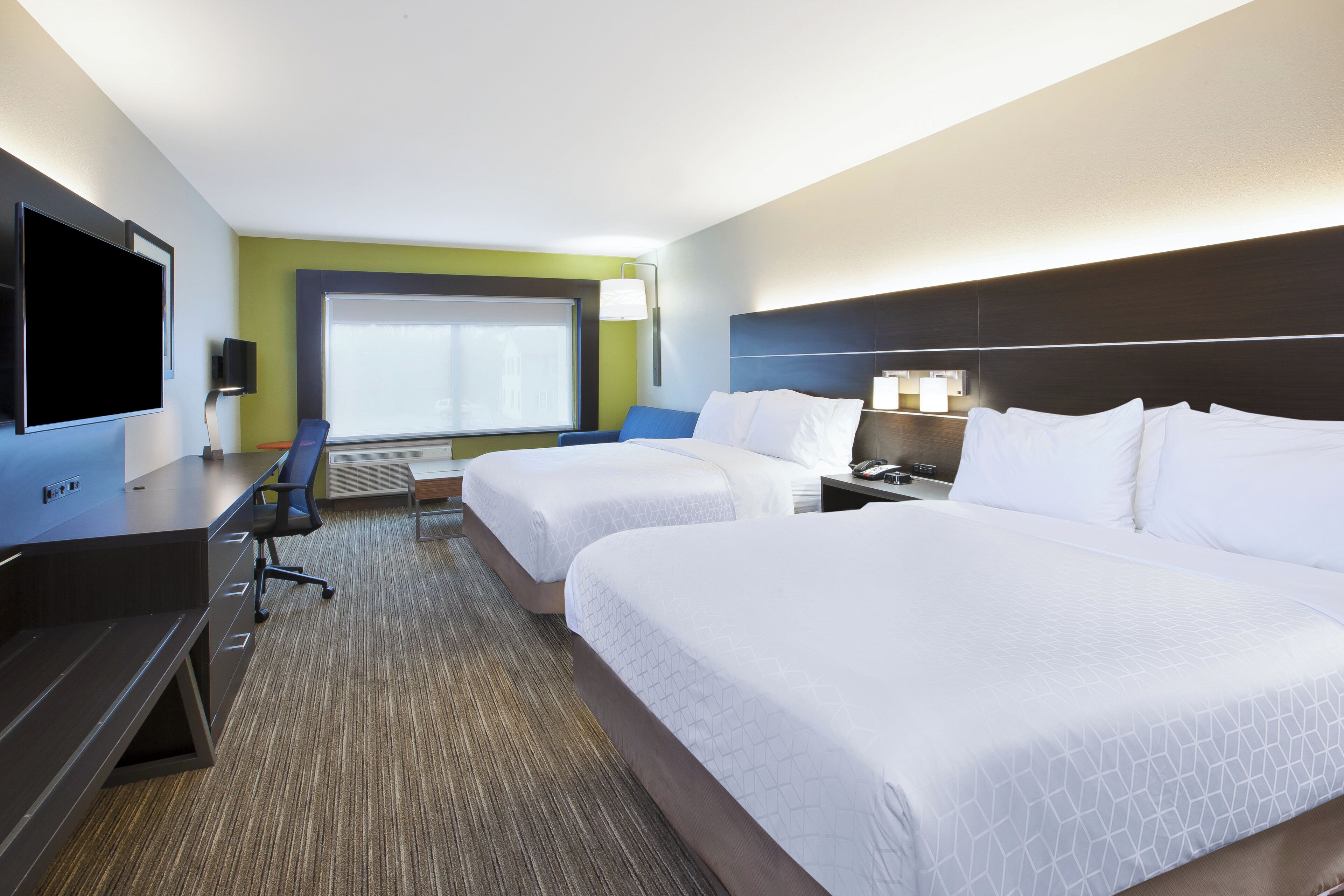 Ein Hotelzimmer mit zwei Betten, einem Schreibtisch, einem Flachbildfernseher, einem Sessel und einem Fenster mit Blick.