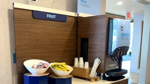 A self-service fruit station with a bowl of fruit, a coffee machine, and a sign that says "Treat Yourself."