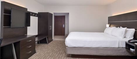 Una habitación de hotel moderna con una cama grande, un televisor montado en la pared, un escritorio con cajones y una puerta que da a otra habitación.