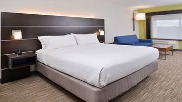 Habitación de hotel con una cama grande, una mesita de noche, un escritorio, una silla azul y un ventanal amplio.