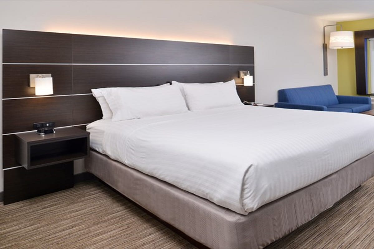 Una habitación de hotel con una cama grande, una mesita de noche, un escritorio, una silla y un ventanal amplio.