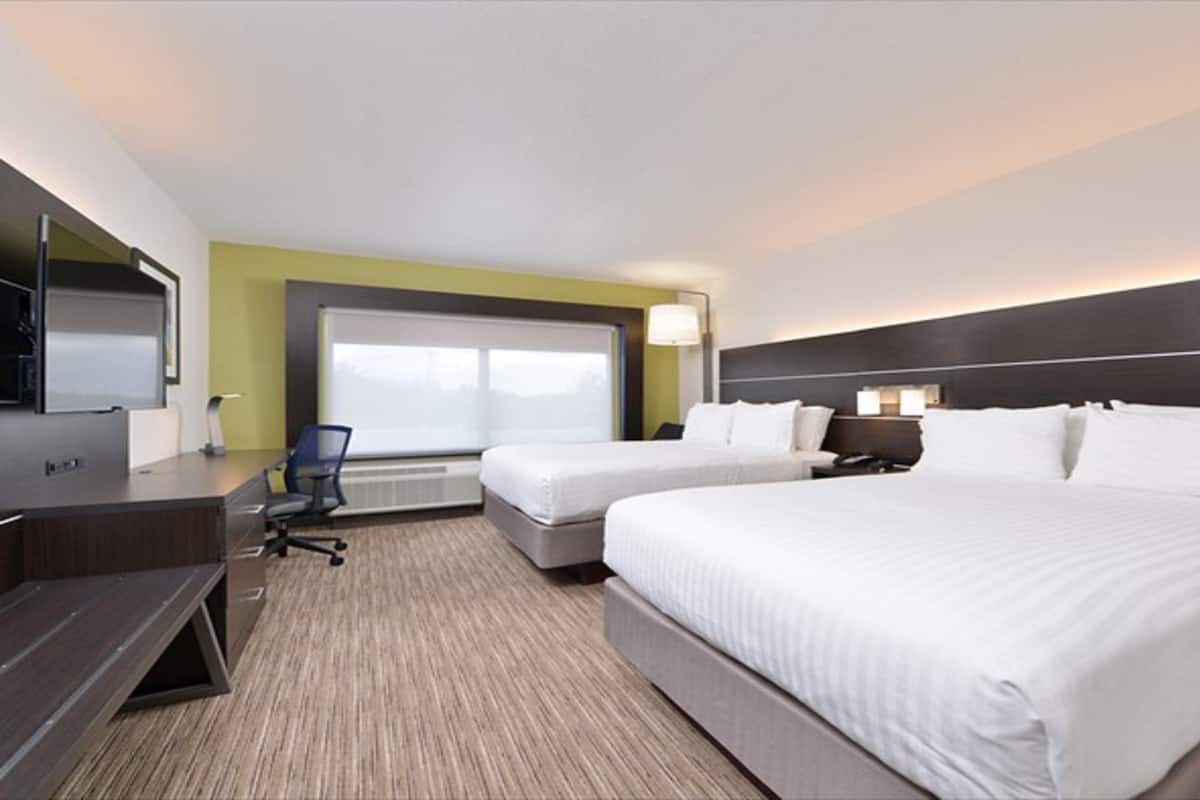A hotel room with two beds, a desk, a chair, a TV, and a window.