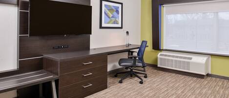 A modern office space with a dark wood desk, a large flat-screen TV, a framed abstract art piece, a blue office chair, and a large window with a view of buildings.