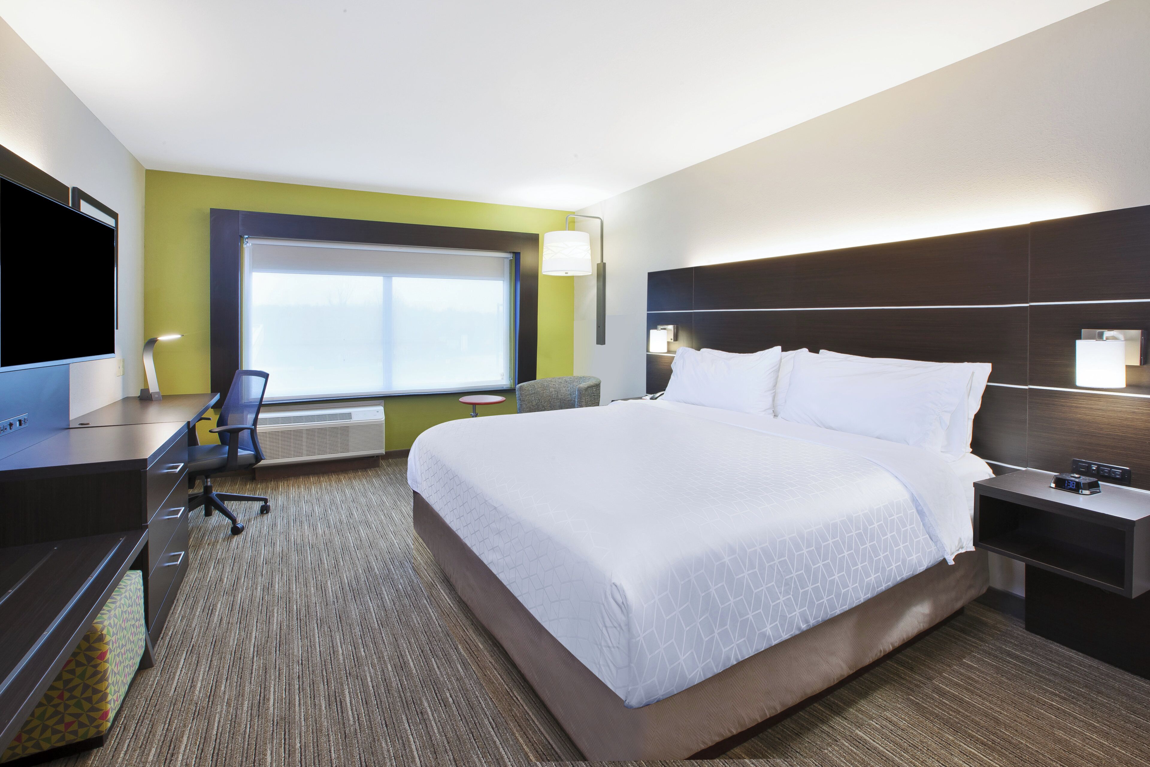 Een hotelkamer met een groot bed, een bureau met stoel, een televisie en een raam met jaloezieën.