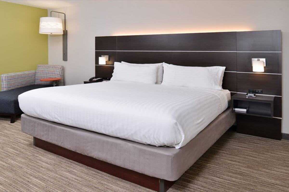 A hotel room with a large bed, a nightstand, a chair, and a lamp.