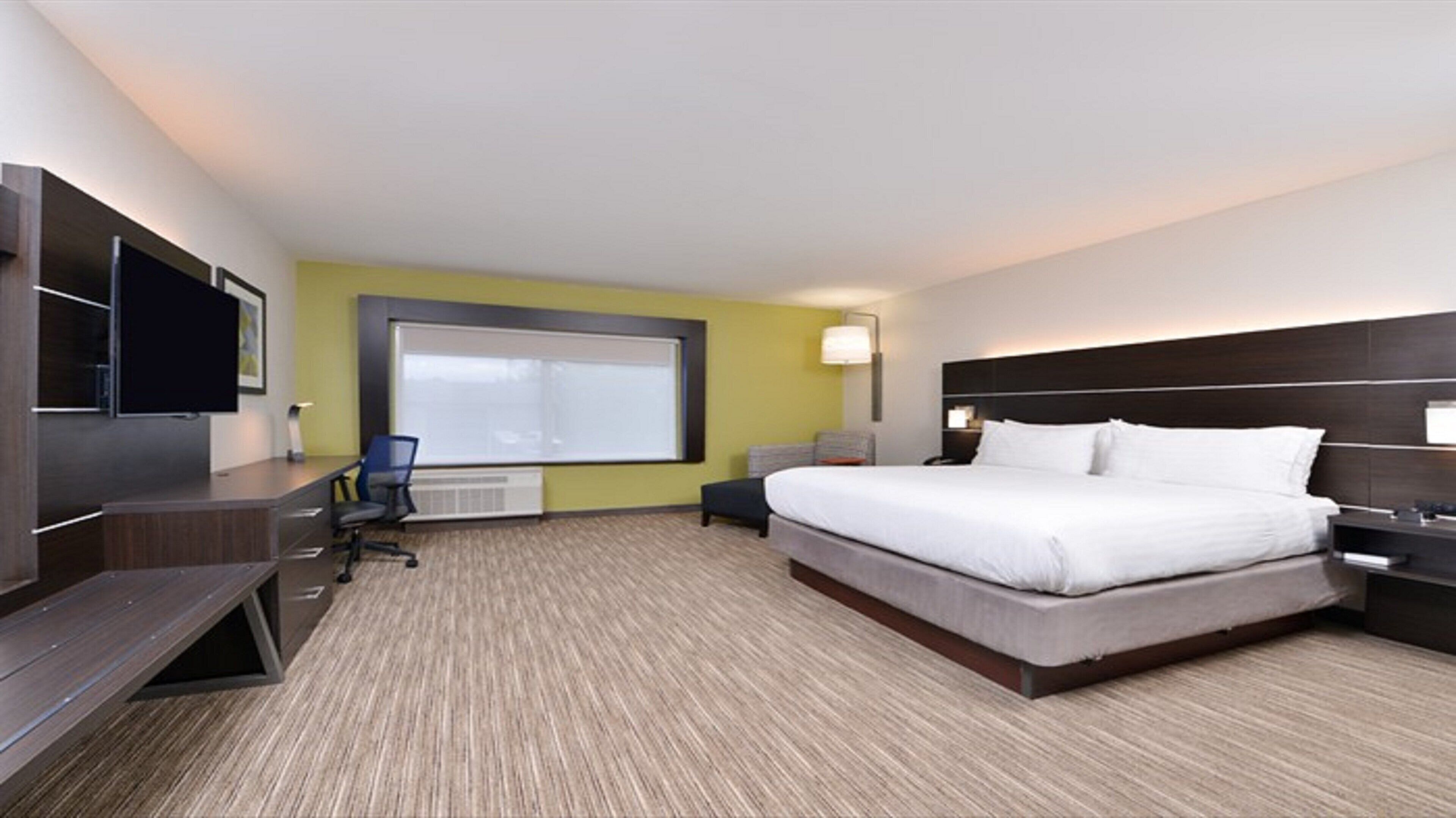 Een hotelkamer met een groot bed, een bureau met een stoel, een televisie en een raam.