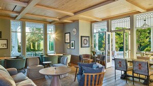A spacious room with a wooden ceiling, large windows with decorative glass, and a variety of seating arrangements including sofas and chairs. - Alila Napa Valley, a Hyatt Luxury Resort (St. Helena)