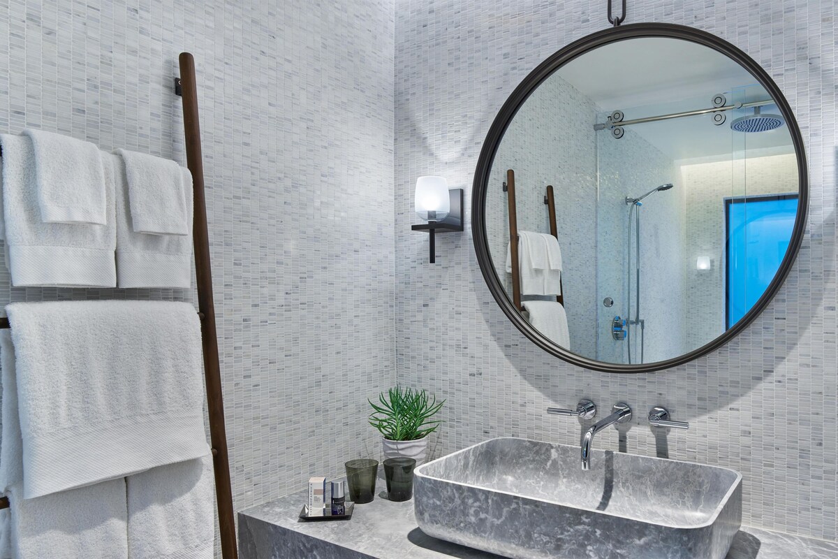 A bathroom with a marble sink, a round mirror, and a towel rack with white towels.