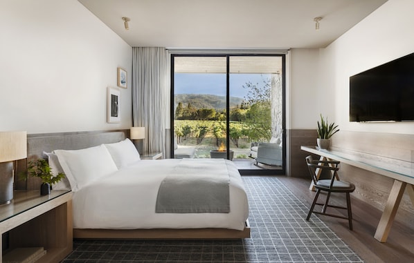 A modern hotel room with a large bed, a desk with a chair, a television, and a view of a vineyard through the sliding glass door. - Alila Napa Valley, a Hyatt Luxury Resort (St. Helena)