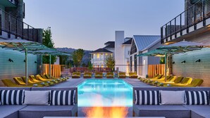 A pool area with lounge chairs, a fire feature, and a view of a building in the background. - Alila Napa Valley, a Hyatt Luxury Resort (St. Helena)