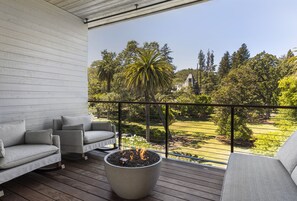 Un balcón con un brasero, dos sofás y vistas a un jardín con árboles y césped.