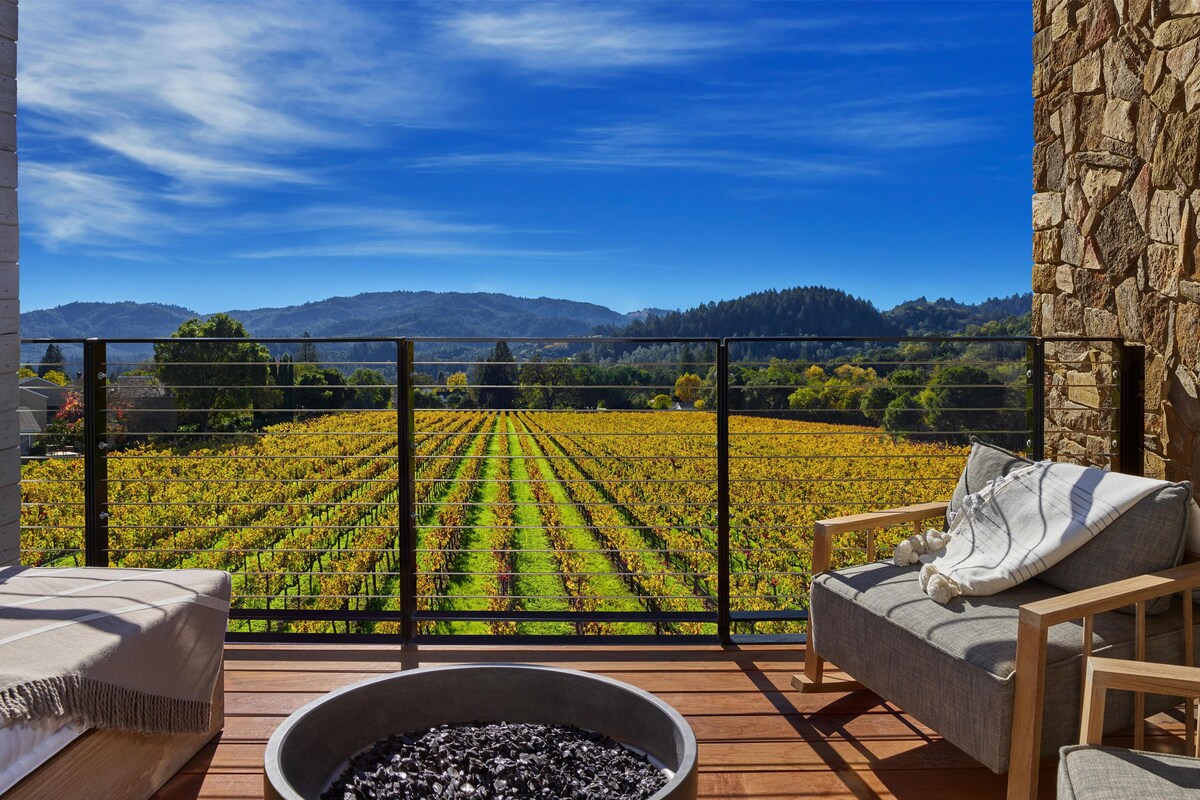 A balcony with a bed, a chair, and a view of a vineyard.
