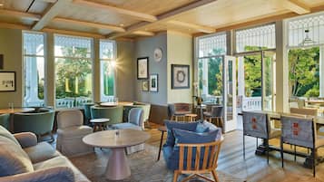 A spacious room with a wooden ceiling, large windows with decorative glass, and a variety of seating arrangements including sofas and chairs.
