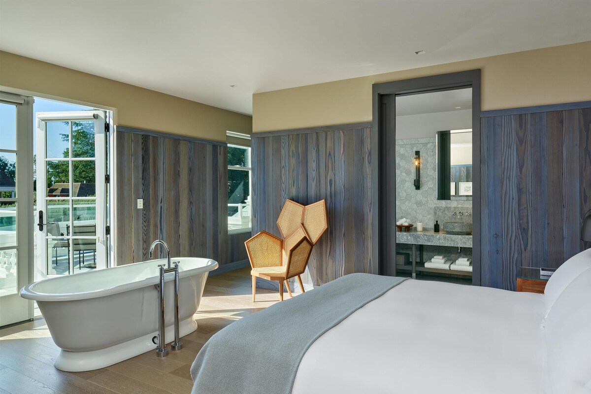 A modern bathroom with a freestanding bathtub, a glass-enclosed shower, and a wooden chair.