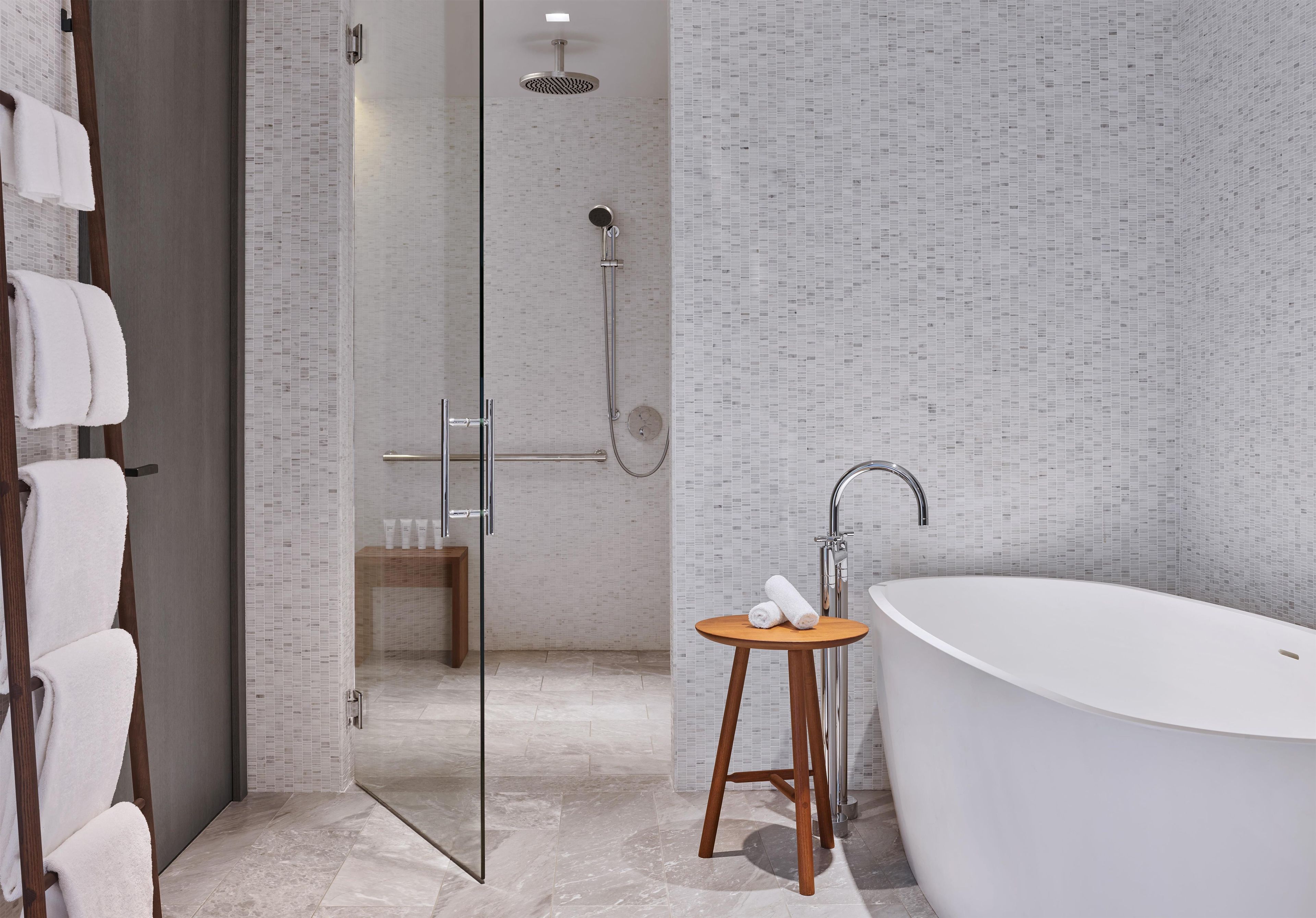 Een moderne badkamer met een douchecabine van glas, een vrijstaand bad en een houten kruk met handdoeken.