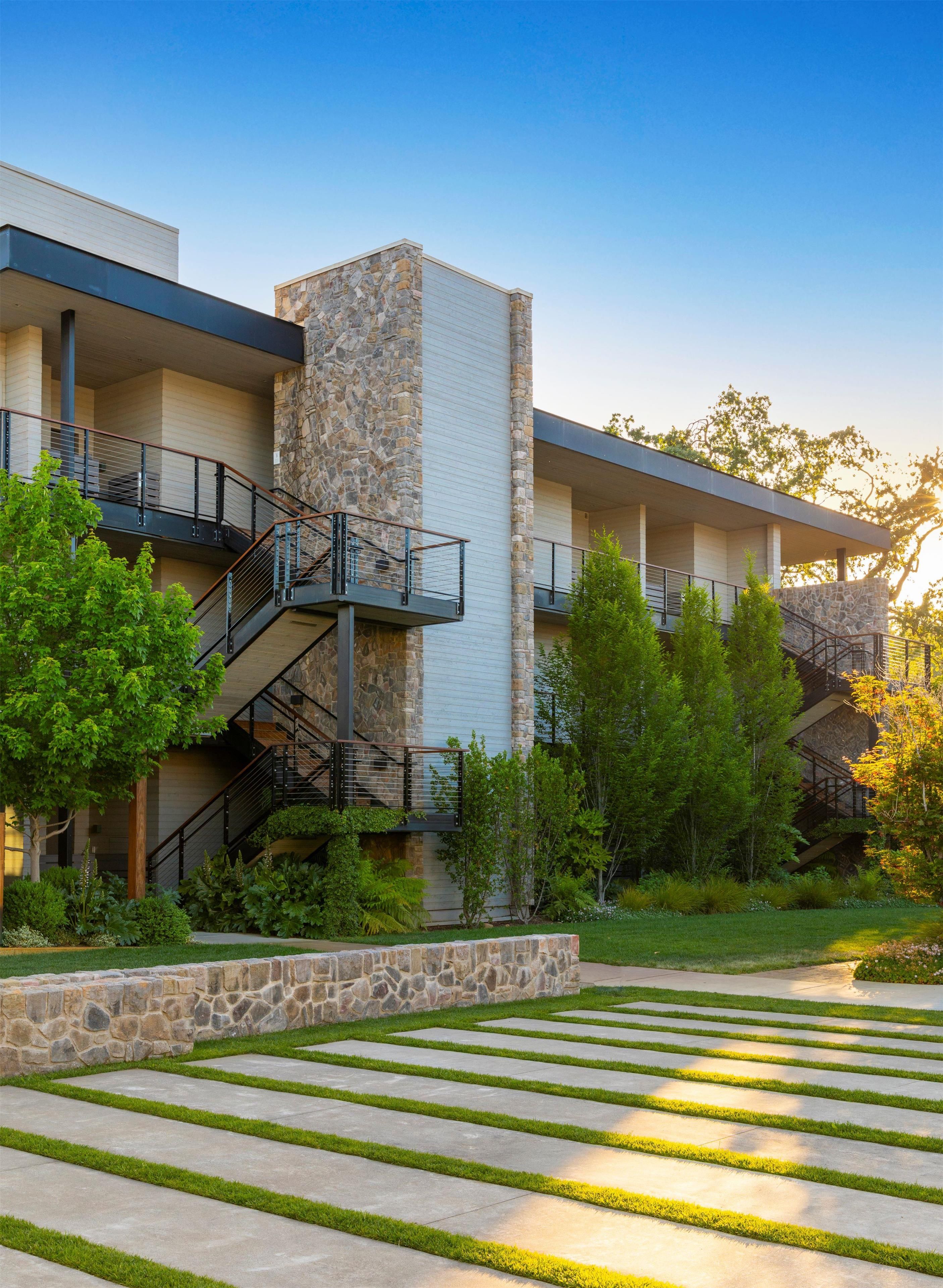 A modern building with a stone facade, multiple balconies, and a landscaped garden with a patterned lawn and stone border.