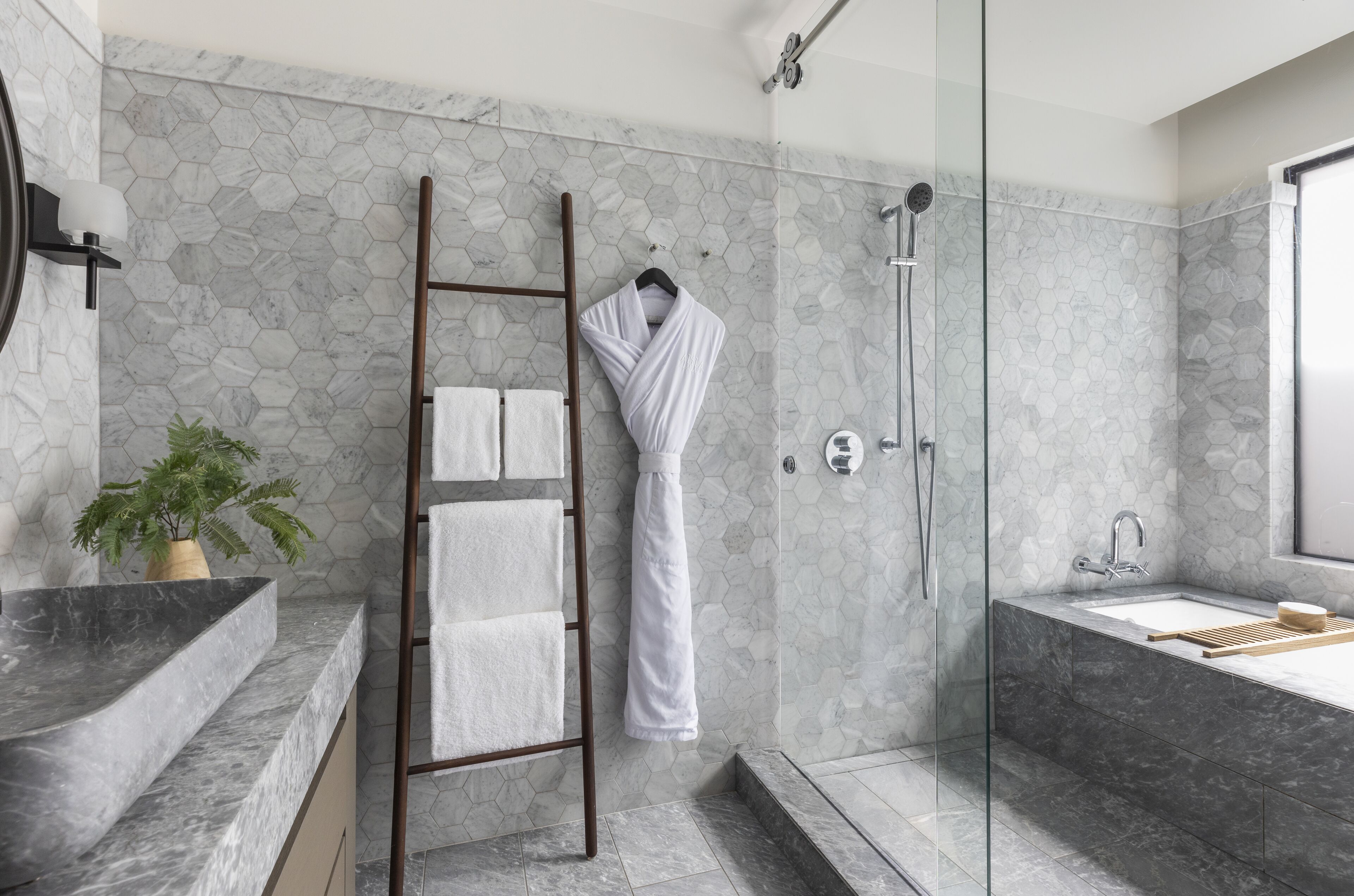 A modern bathroom with a glass shower enclosure, a marble sink, and a wooden ladder.