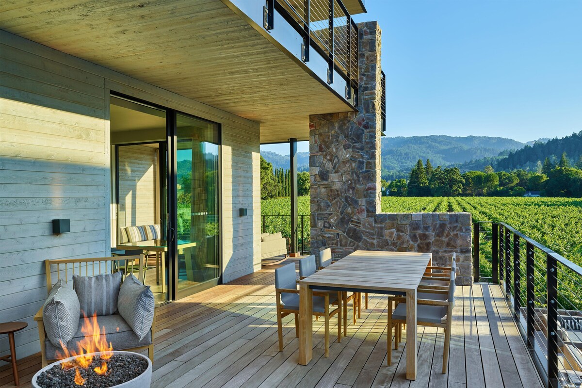 A wooden deck with a fire pit, outdoor seating, and a view of a vineyard.