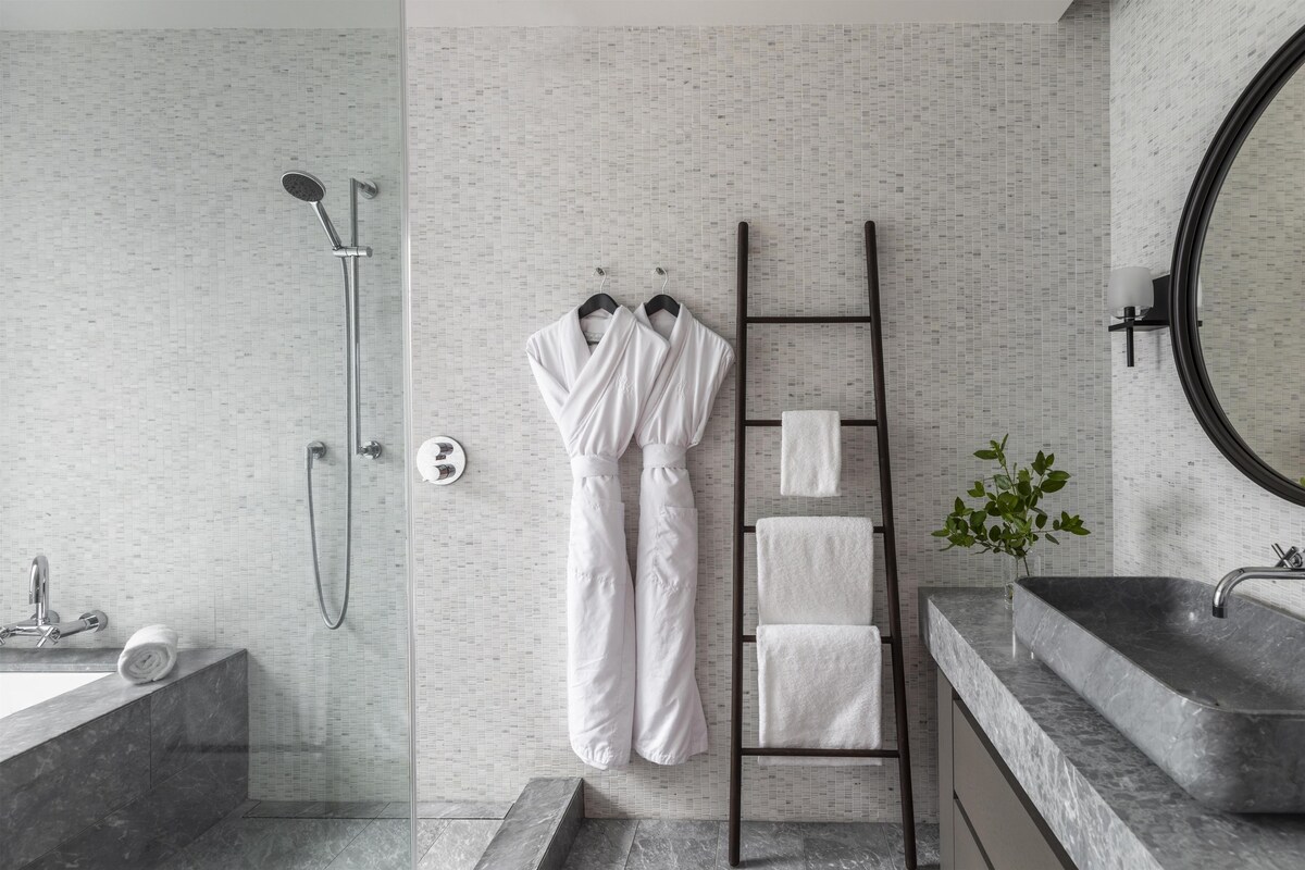 A modern bathroom with a shower, a towel rack, a marble sink, and a mirror.