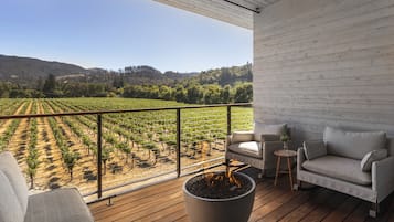 A balcony with a view of a vineyard, a fire pit, and a sofa.