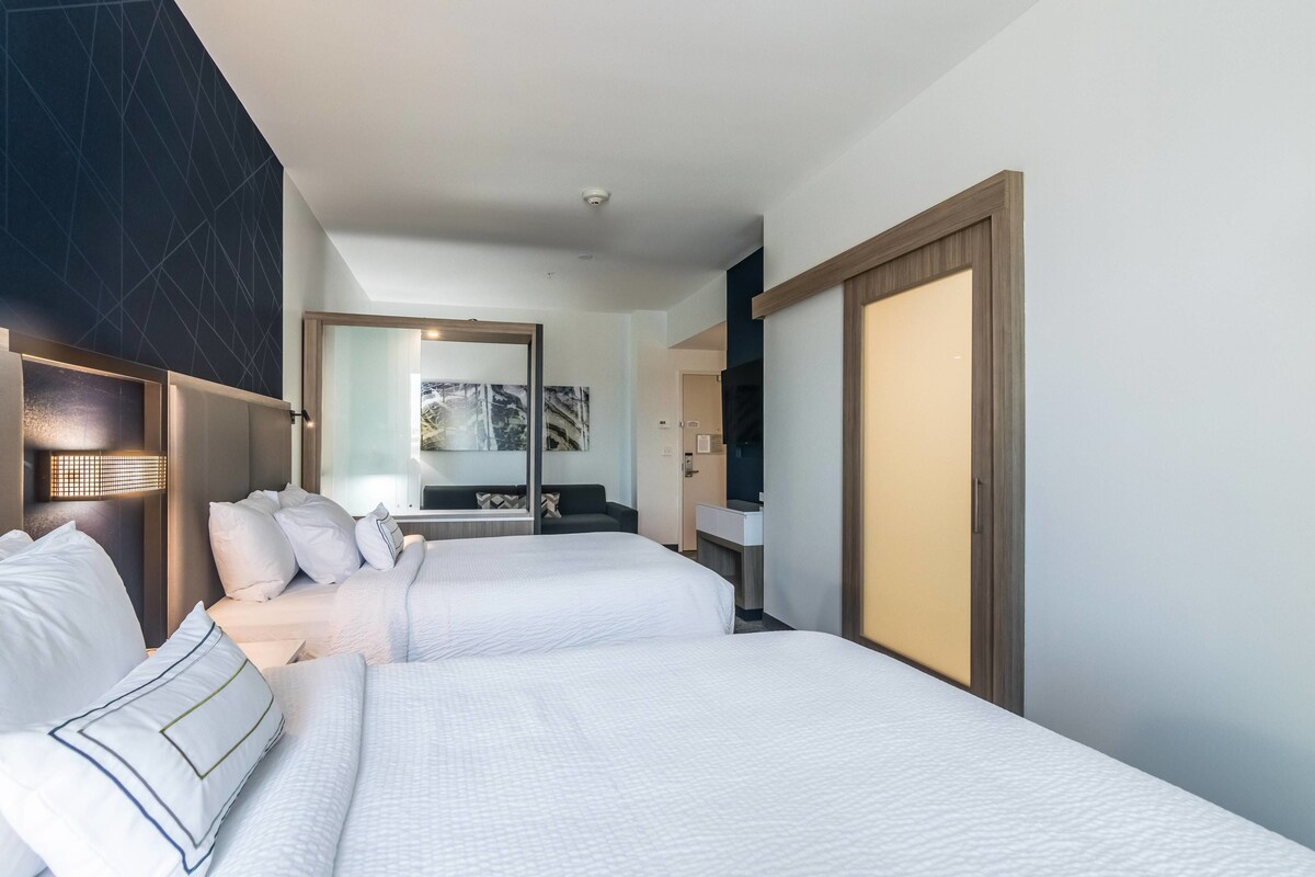 Ein Hotelzimmer mit zwei Betten, einem großen Spiegel, einem Kleiderschrank und einem Badezimmer mit Waschbecken und Spiegel.