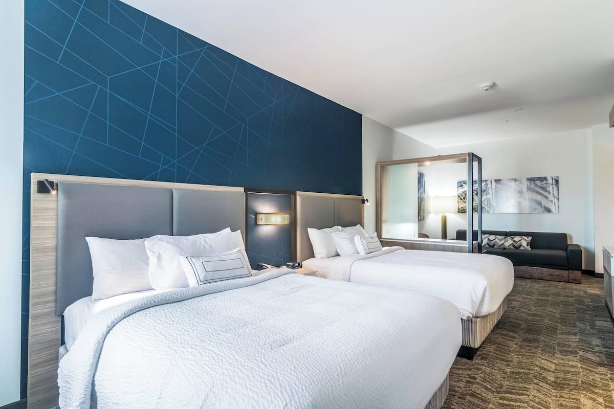 Habitación de hotel con dos camas, un sofá, un espejo grande y una pared con un diseño geométrico.
