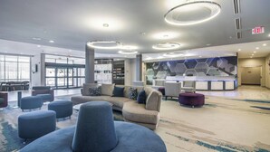 A spacious lobby with a large curved sofa, multiple ottomans, a reception desk, and a modern geometric wall design. - SpringHill Suites by Marriott Oklahoma City Downtown (Oklahoma City)