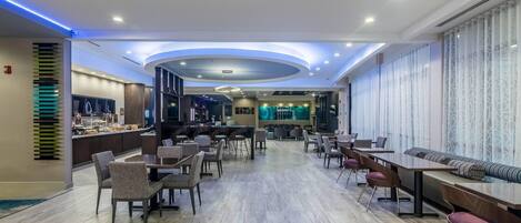 Un amplio vestíbulo de hotel con una zona de bar central, diferentes disposiciones de asientos y un diseño de techo moderno.