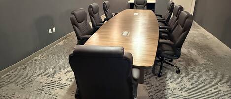 A conference room with a large rectangular table, black chairs, patterned carpet, and a ceiling light fixture.