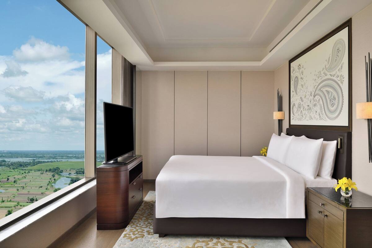 Een moderne hotelkamer met een groot bed, een televisie, een nachtkastje en uitzicht op een groen landschap.