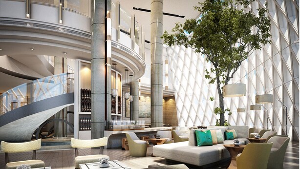 A modern hotel lobby with a curved staircase, seating areas, and a large tree.