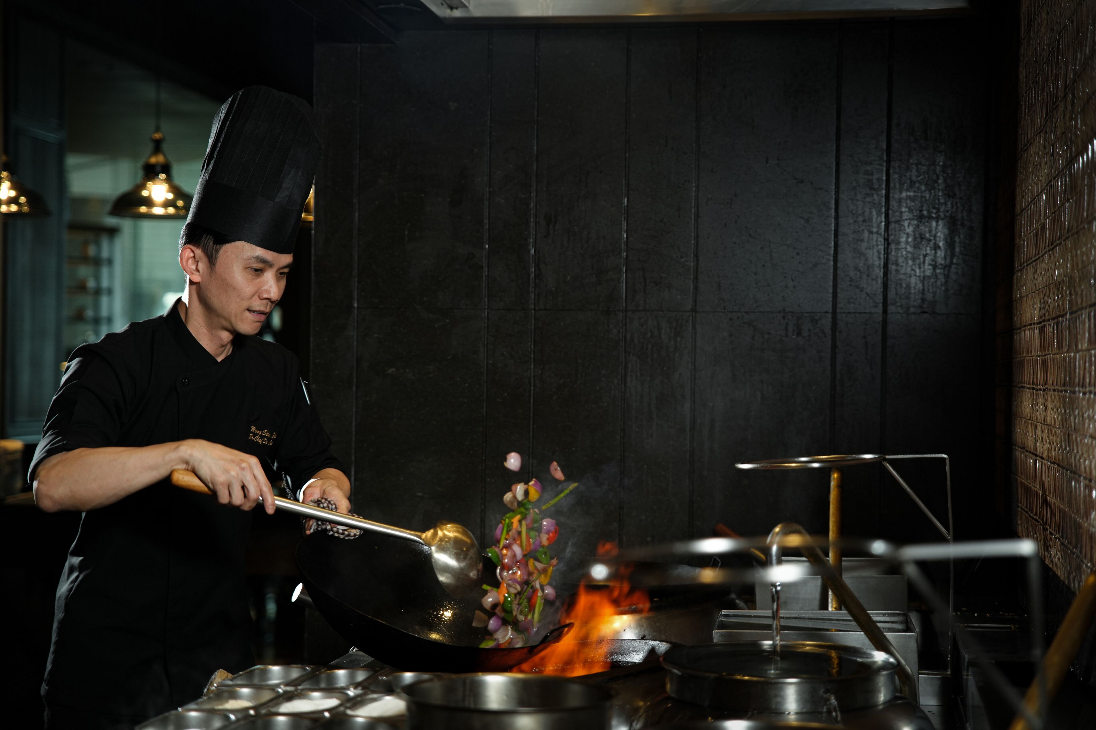 A chef cooking with a wok over an open flame in a kitchen.