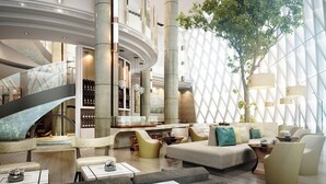 A modern hotel lobby with a curved staircase, seating areas, and a large tree.