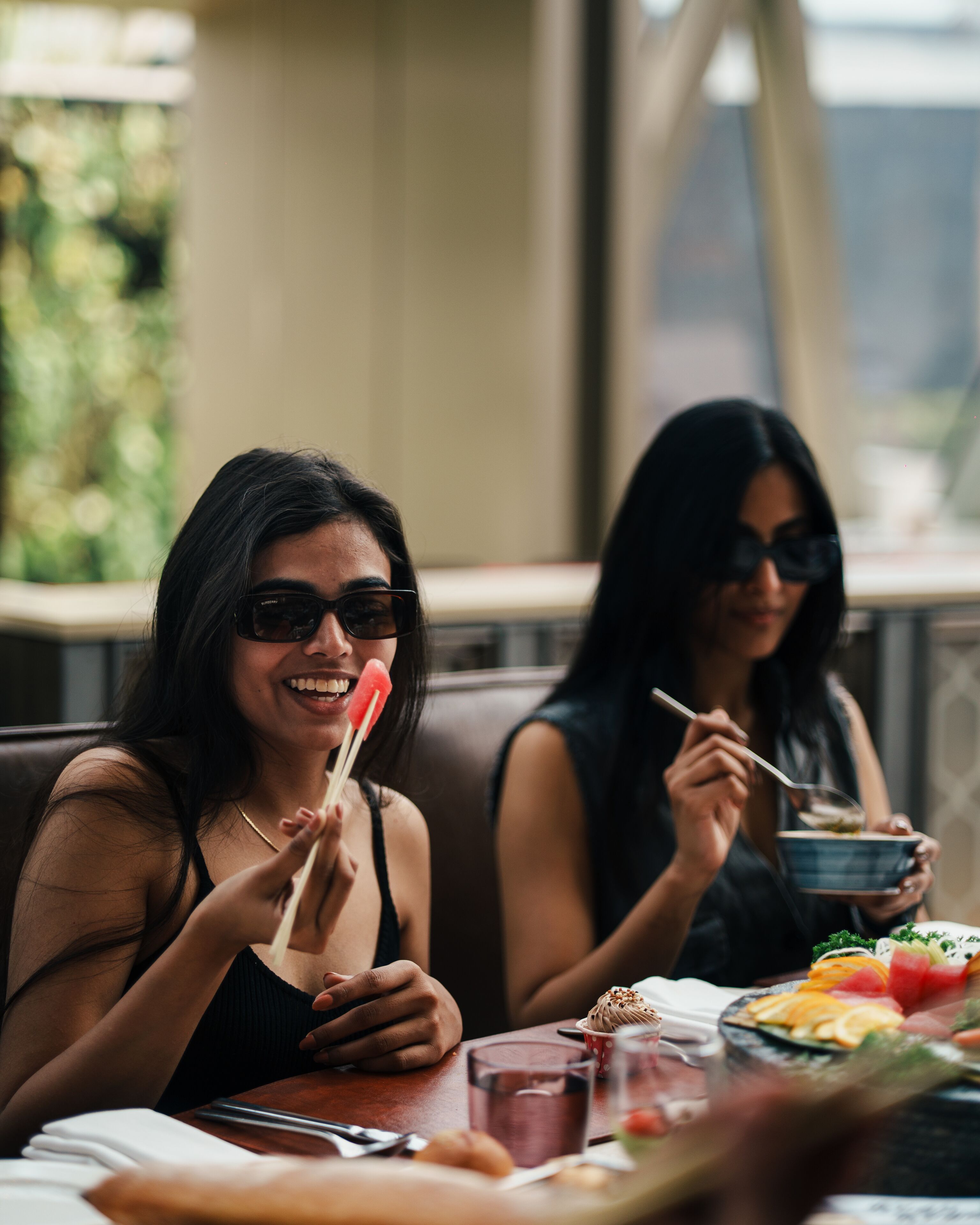 Dos personas cenando en un restaurante al aire libre, con una mesa preparada para la comida, incluyendo un bol y un plato con alimento.