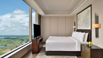 A modern hotel room with a large bed, a flat-screen TV, a nightstand, and a view of a landscape through a large window.