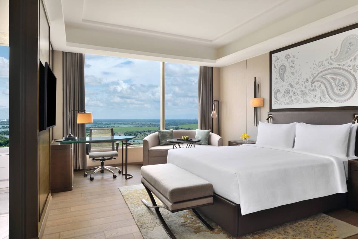 Een moderne hotelkamer met een groot bed, een bureau met een computer, een comfortabele fauteuil en uitzicht op de stad.