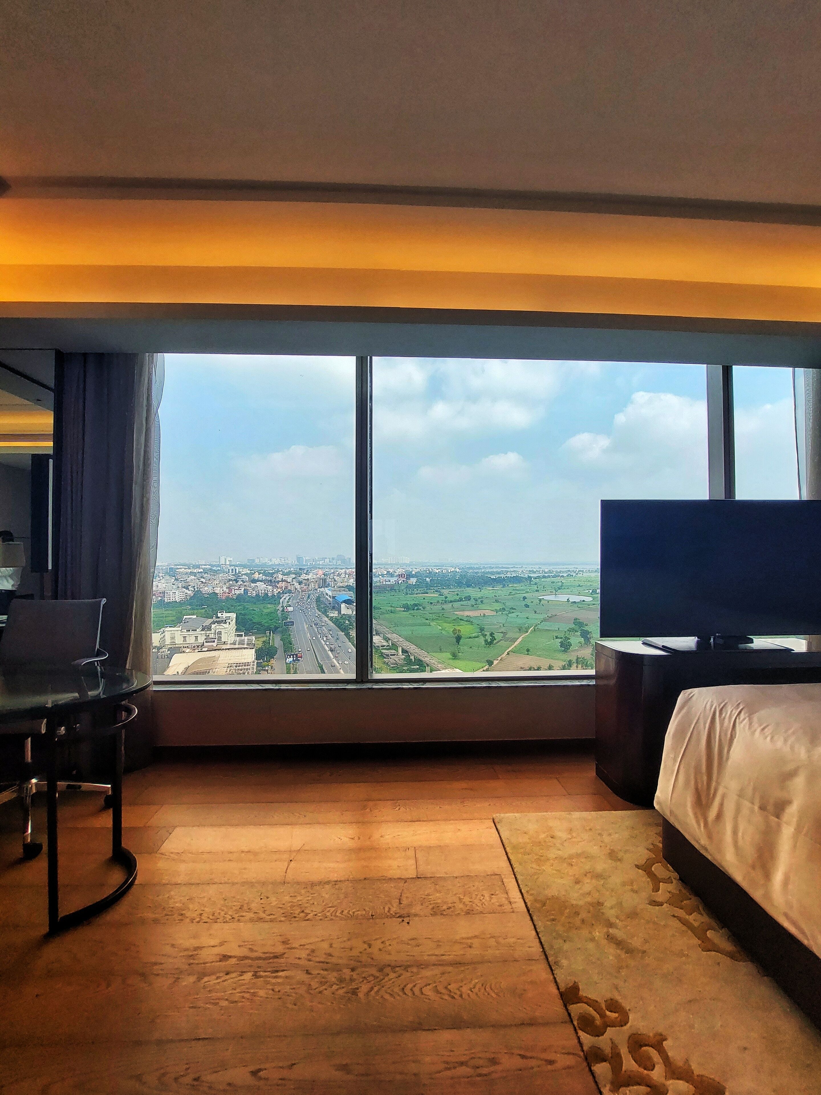 A hotel room with a large window, a bed, a TV, and a desk with a chair.