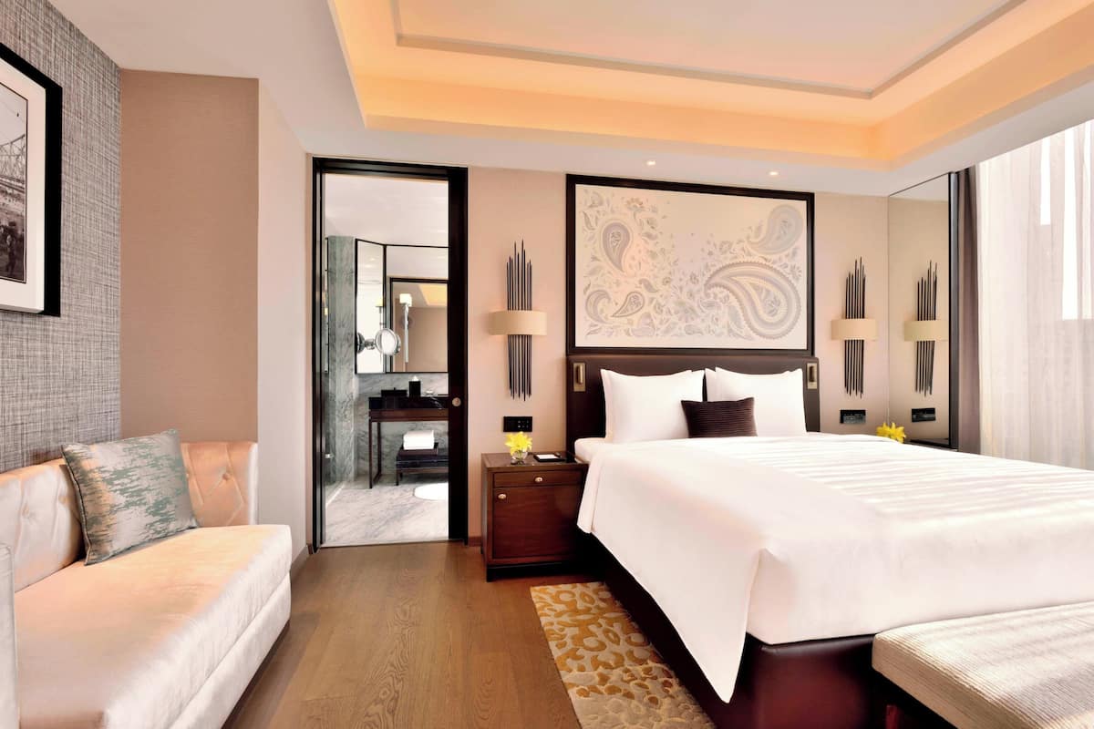 Een moderne hotelkamer met een groot bed, een bank, een bureau en een badkamer die door een open deur zichtbaar is.