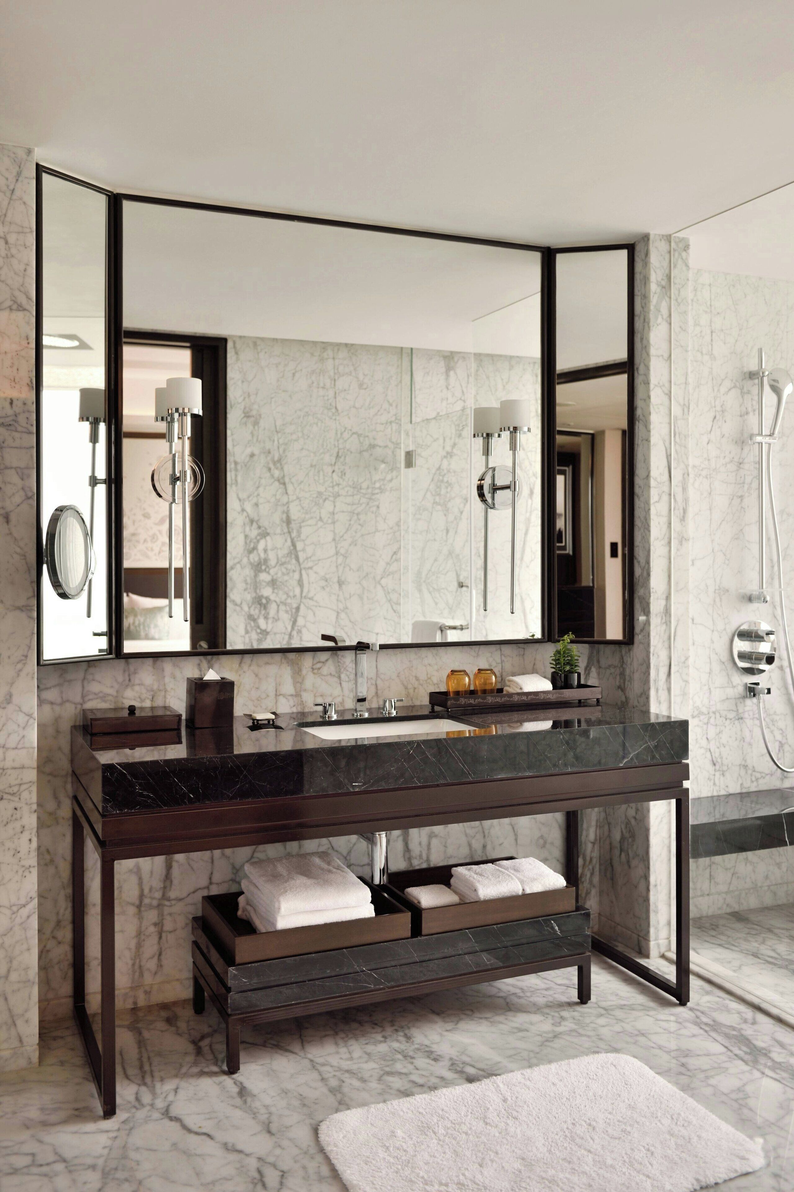 A modern bathroom with a dark wooden vanity, a large mirror, and a marble backsplash.