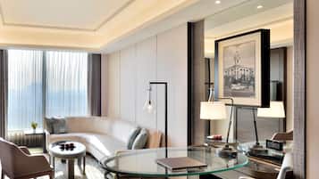 Habitació d'hotel moderna amb taula de vidre, un sofà, una cadira i escriptori amb làmpada.