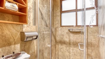 Un baño con cabina de ducha de vidrio, paredes de mármol, un perchero y una ventana con vidrio esmerilado.