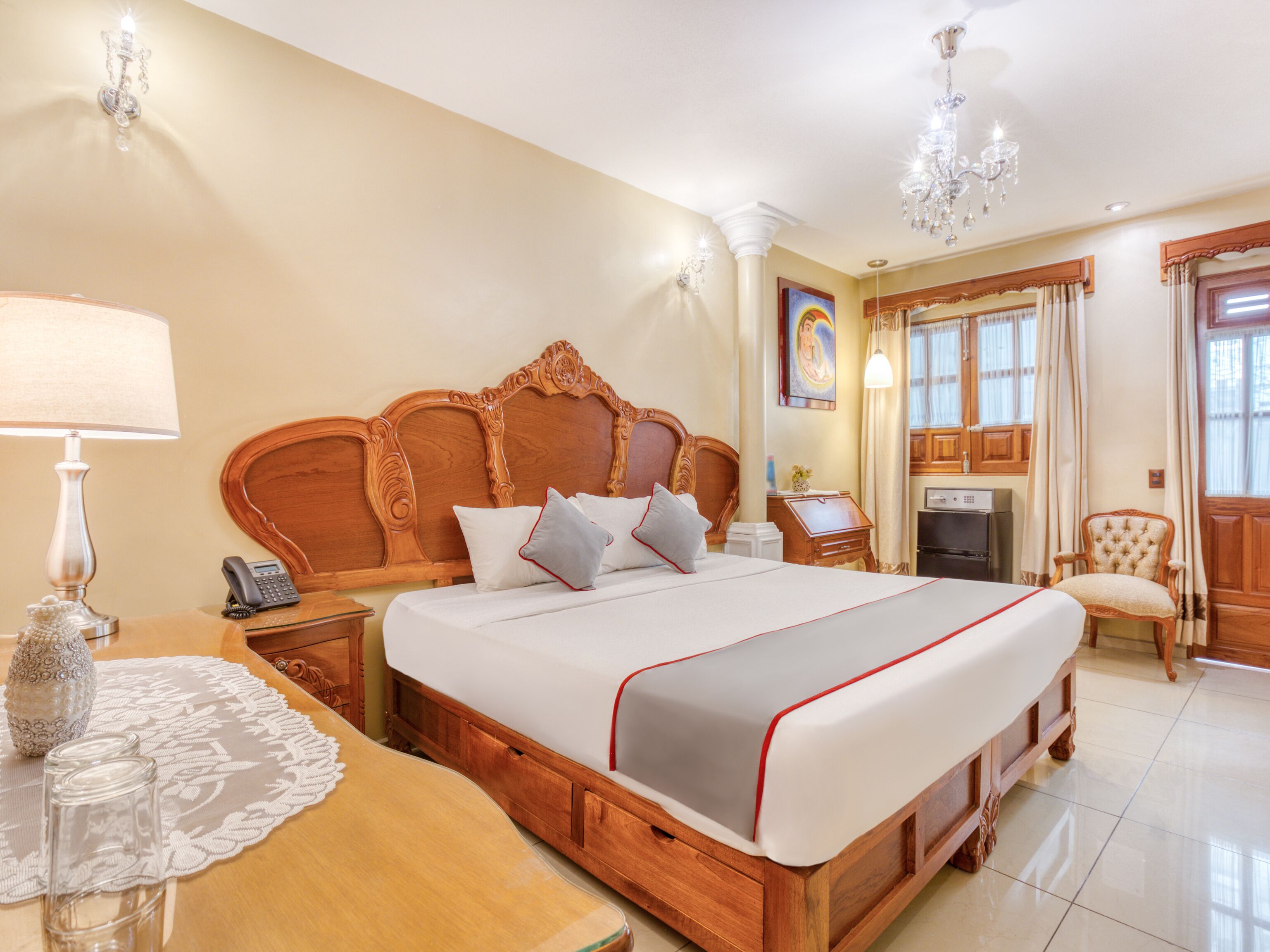 A hotel room with a large bed, wooden headboard, bedside tables, a lamp, a telephone, a decorative vase, and a chair.