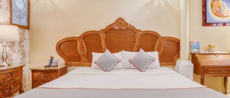 A large bed with a wooden headboard, two bedside tables, a lamp, and a painting on the wall.