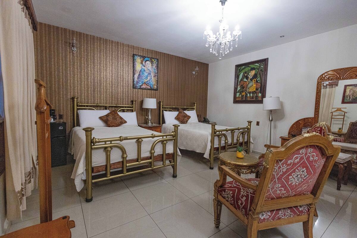 A hotel room with two beds, a chandelier, a dining table with chairs, and artwork on the walls.