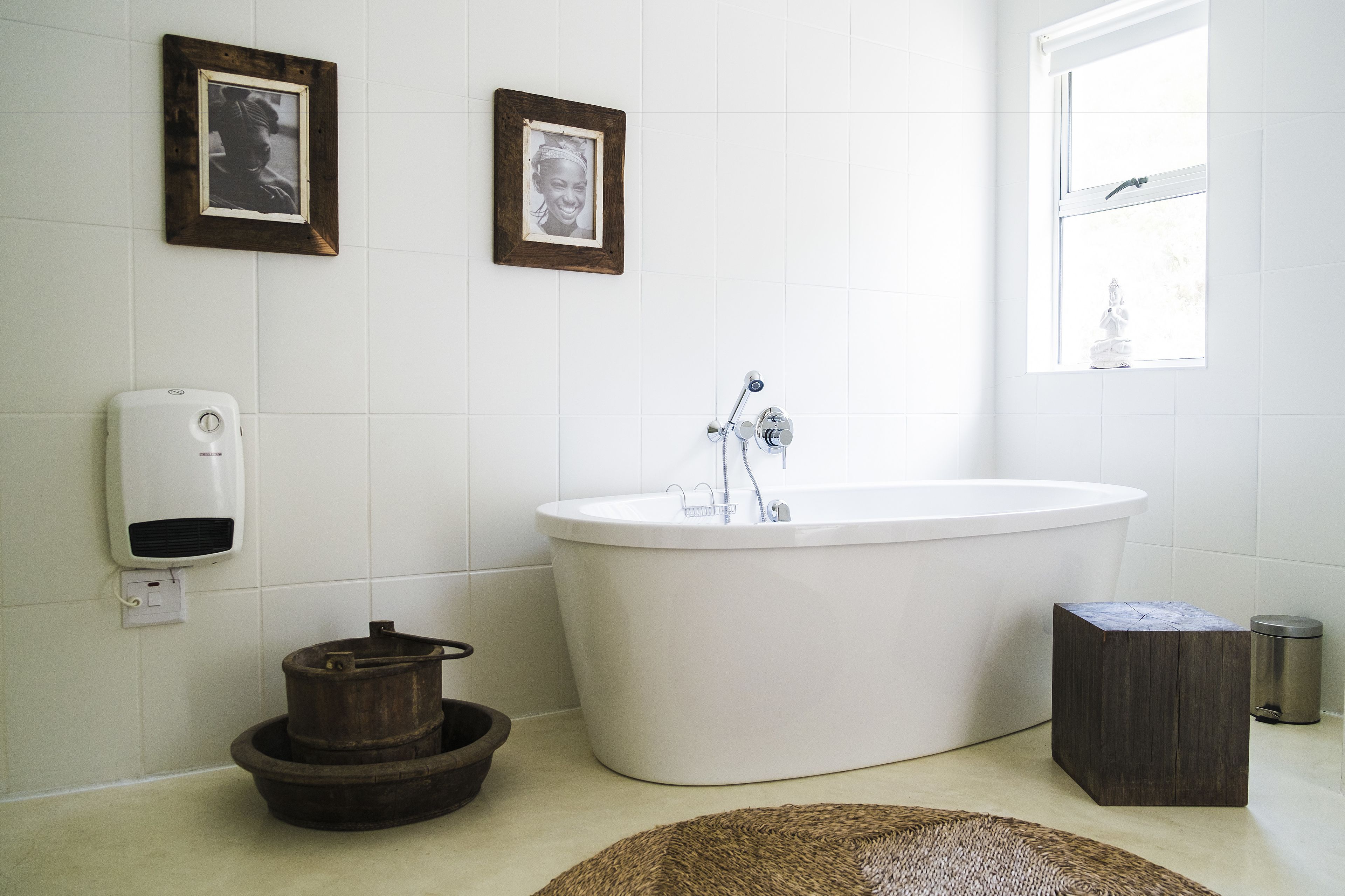 A bathroom with a freestanding bathtub, a wooden bucket, a soap dispenser, and two framed pictures on the wall.
