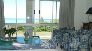 A room with a large window offering a view of the ocean, a sofa, a table with a vase of flowers, and a lamp.